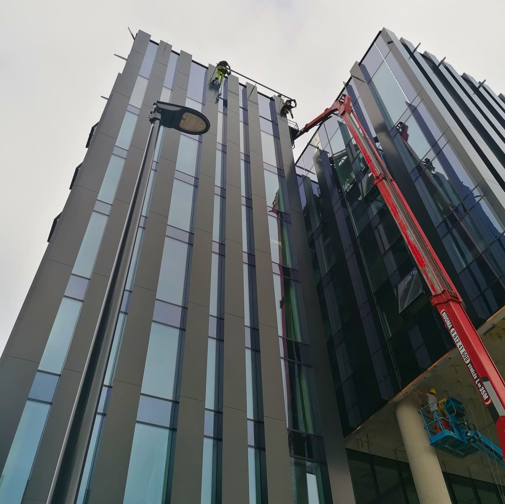 Vyras ant kėlimo platformos dirba prie pastato sienos, demonstruodamas statybos ar remonto darbus.