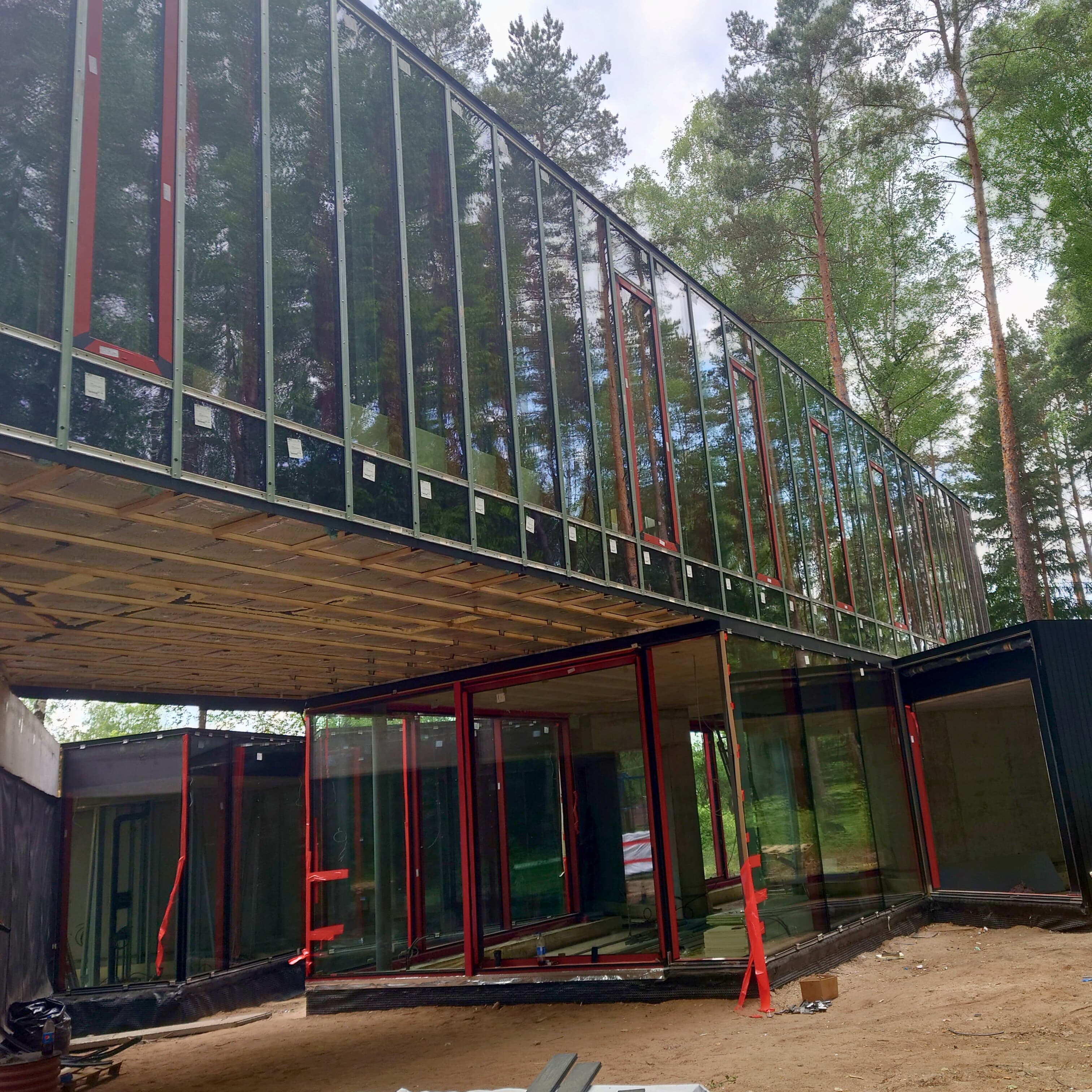 Iš dalies pastatytas stiklinis namas, apsuptas pastolių ir statybinės įrangos, rodantis vykstančius statybos darbus.